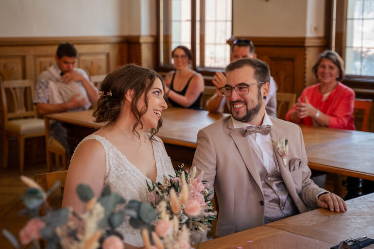 Hochzeitsfotograf Allgäu und Kempten. Schwarz-weiß-Bild vom Brautpaar. Das Brautpaar sitzt im Standesamt. Die beiden sehen sich an und lachen.