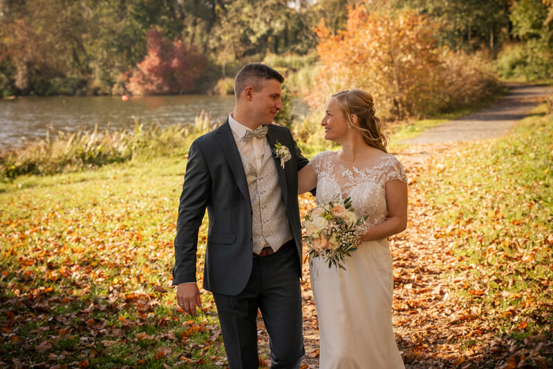 Hochzeitsfotograf Allgäu und Kempten. Ein Brautpaar in der Herbstsonne geht nebeneinander und sieht sich dabei in die Augen. Die Braut hält den Brautstrauß vor sich.